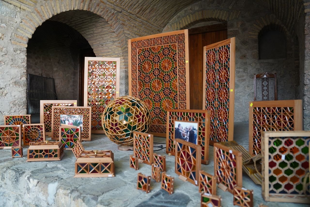 gallery-4 Intricately designed wooden crafts with colorful geometric patterns displayed in a rustic setting.
