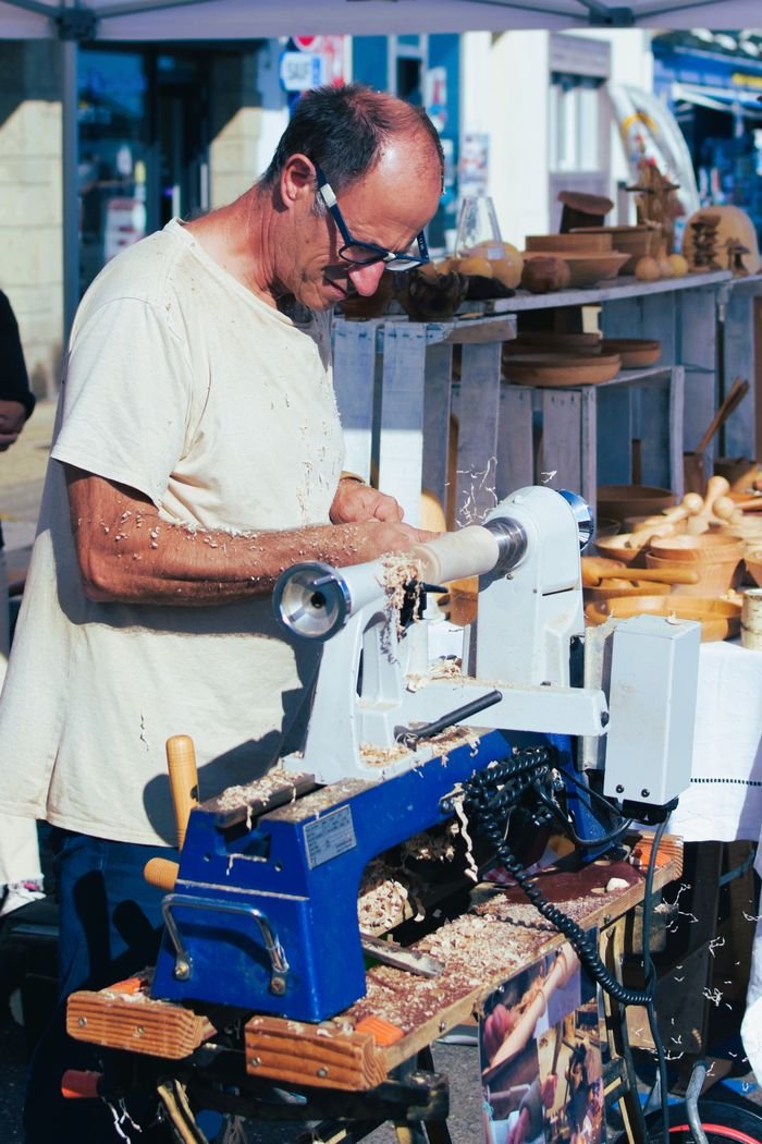 about-01 A skilled craftsman using a lathe to create wooden bowls at a lively outdoor market in Camaret-sur-Mer, France.