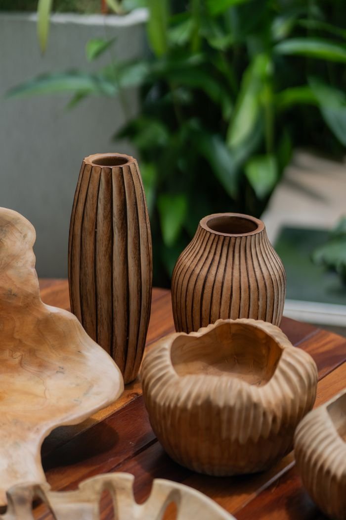 services-01 Artistic arrangement of handmade wooden vases on a wooden table with foliage backdrop.