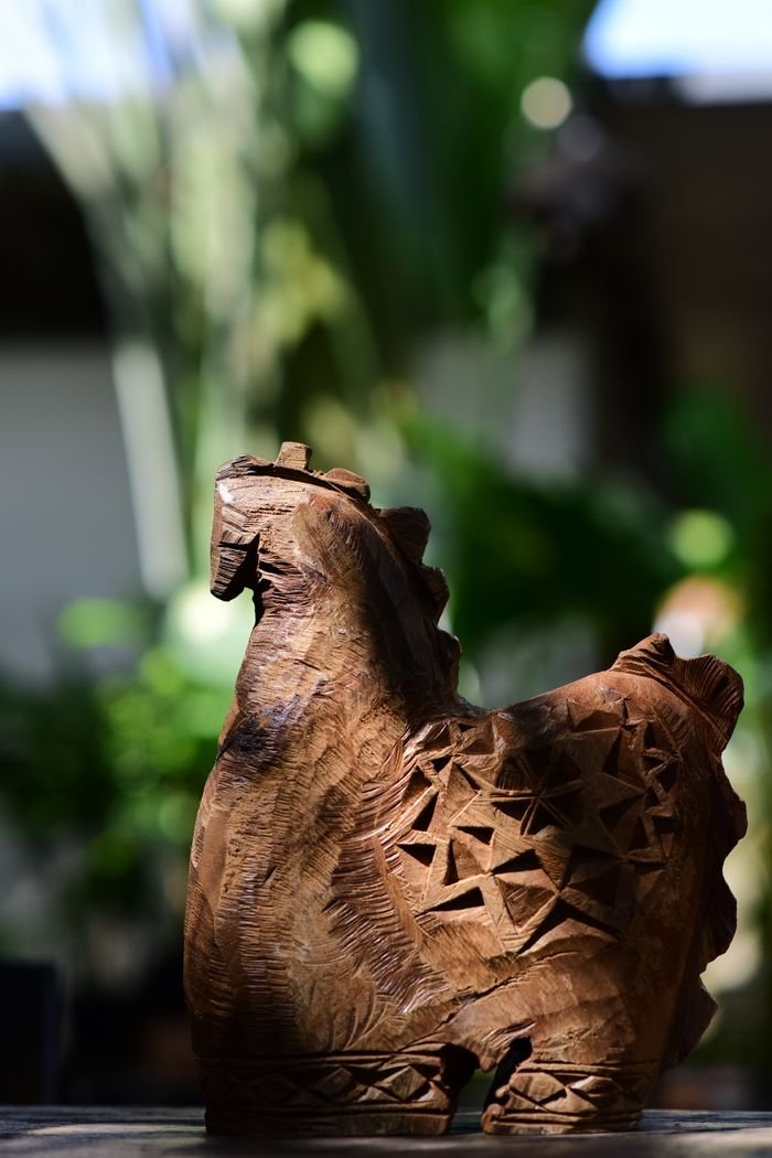 A beautifully carved wooden animal sculpture with intricate patterns, set outdoors in a natural environment.