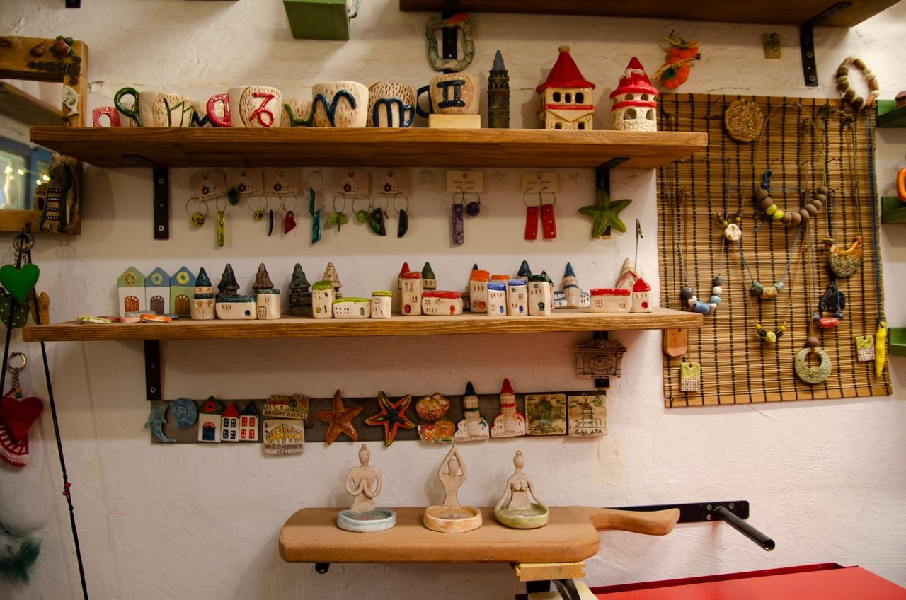 services-01 A vibrant collection of handmade ceramic pottery and trinkets neatly arranged on wooden shelves, creating a warm and artistic ambiance.