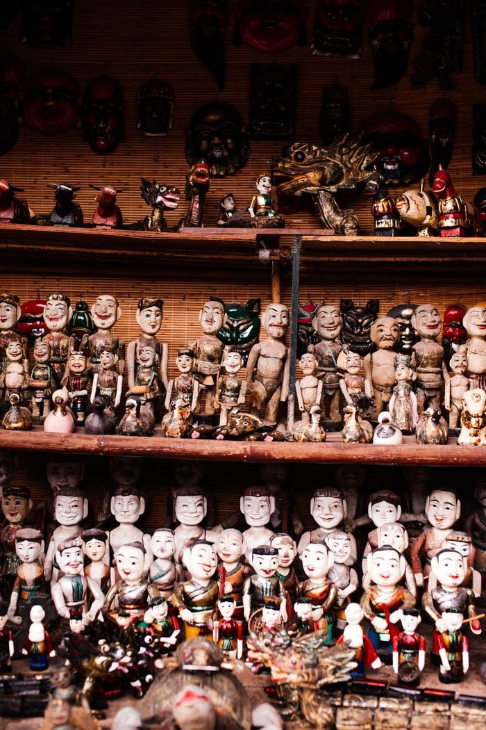 services-img A collection of ethnic handmade dolls exhibited on wooden shelves in a cultural shop.